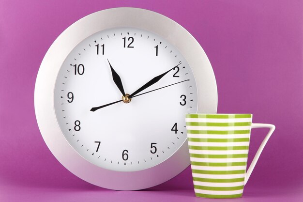Cup tea and clock on purple background