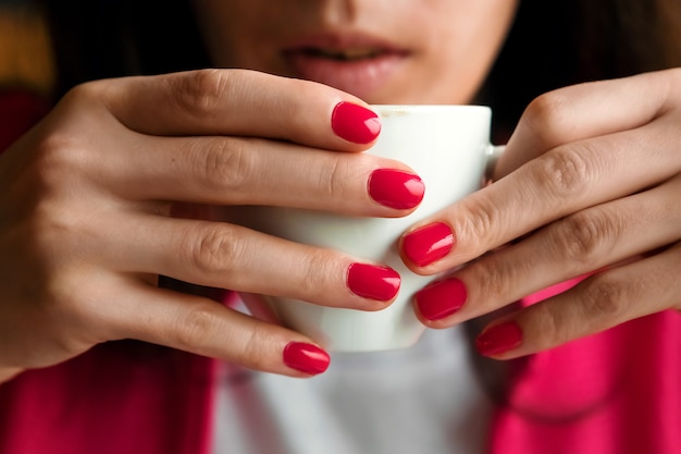 Чашка чая или кофе в руках женщины, розовый маникюр, крупный план