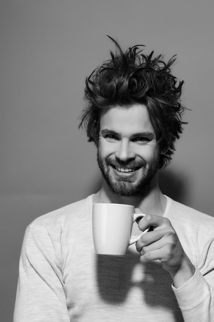 Photo cup of tea or coffee at happy man with uncombed hair in underwear on red background, morning refreshment and drink, energy