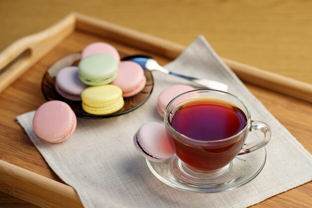 Photo cup of tea and colorful macaroons on a wooden tray morning tea and sweets