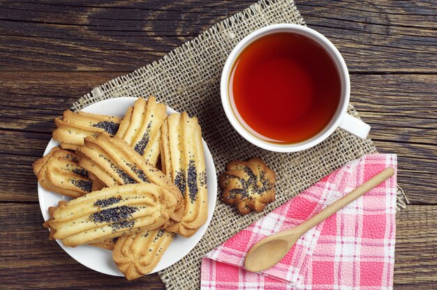 Cup of tea and cookies with poppy on wooden table, top view