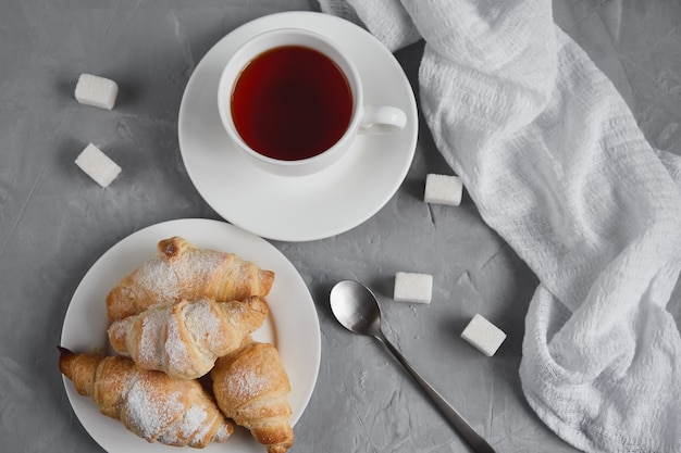 Cup of tea, croissants, sugar cubes on a gray background, breakfast concept, view from above