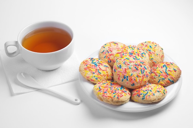 Tazza di tè e deliziosi biscotti con granelli colorati in piatto su sfondo bianco