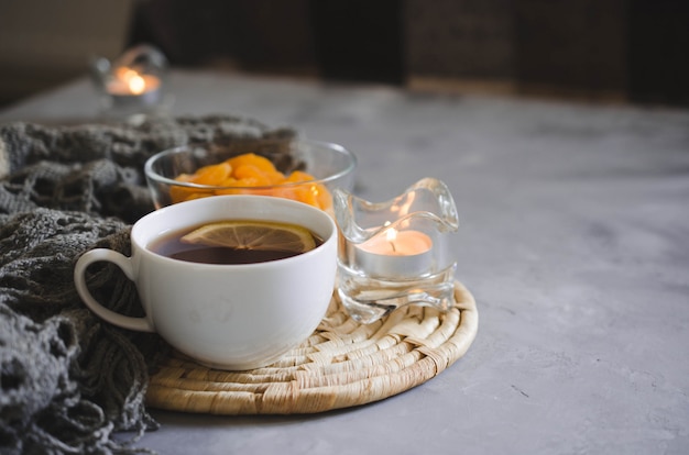 Cup of tea and dried apricots on a table, candles and knited blanket.