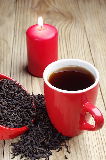 Cup of tea and dry black tea and burning candle on a wooden table