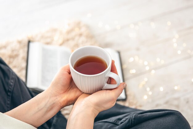 女性の手の茶のカップ部屋の床のカーペット上のクローズアップブック