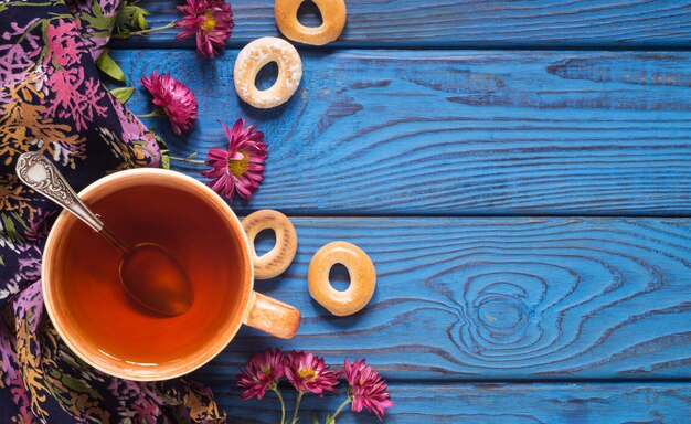 青い木製のテーブルの背景にお茶、花、ベーグルのカップ