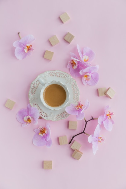 cup of tea and flying orchid flowers on light pink