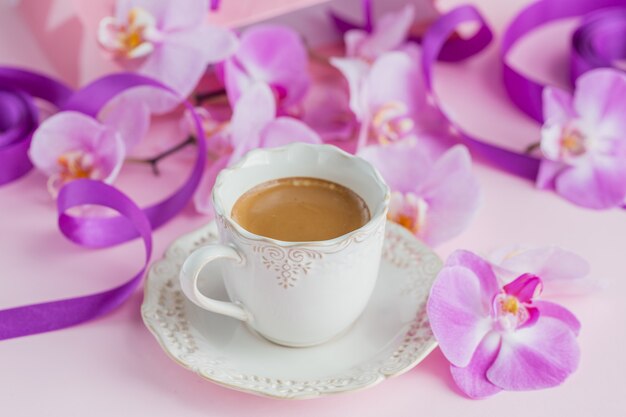 cup of tea and flying orchid flowers on light pink