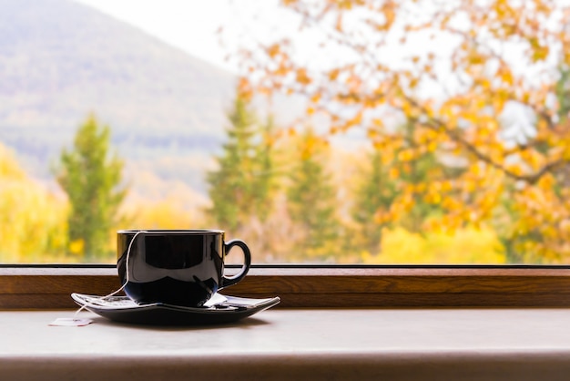 Photo a cup of tea in front of a window with autumn view.