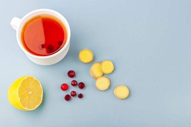 Cup of tea, ginger, lemon and cranberry as folk remedies on blue