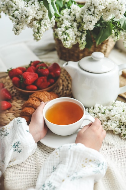 Cup of tea in hands strawberries and flowers summer breakfast concept