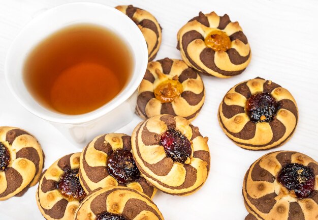 Cup of tea and heap of cookies with jam on white wooden table Top view