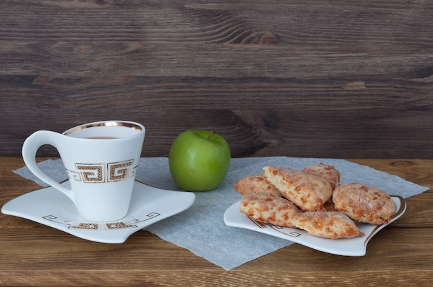 Una tazza di tè, biscotti fatti in casa e una mela su uno sfondo di tavole di legno.