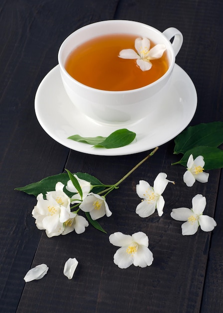 Cup of tea and jasmine flowers on dark wooden background.