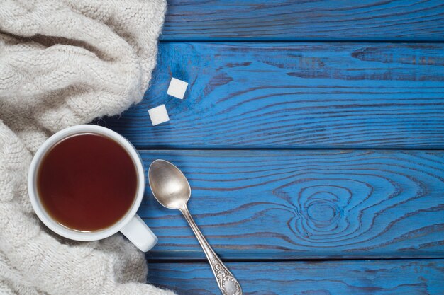 A cup of tea and a knitted scarf on the background of blue wooden table