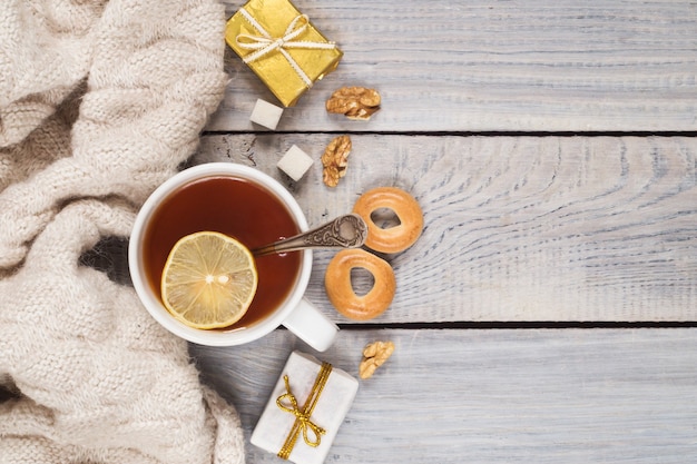 A cup of tea, a knitted scarf and gifts on the background of white wooden table