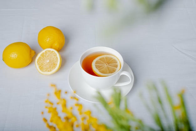 Tazza di tè e limone con fiore di mimosa su una vista da tavolo bianca