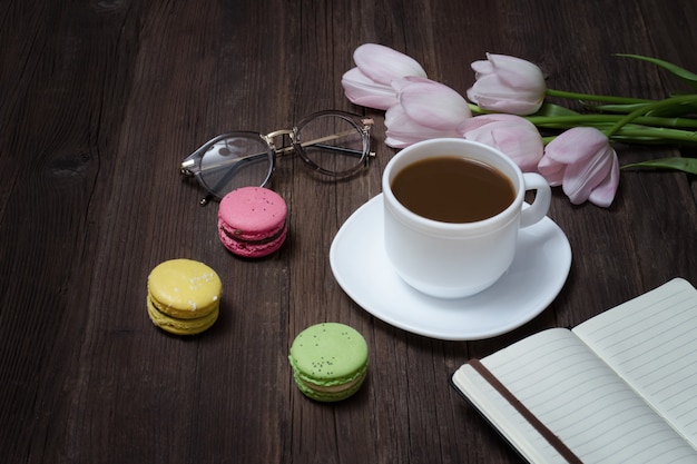 Cup of tea, macarons, glasses, pink tulips and notebook