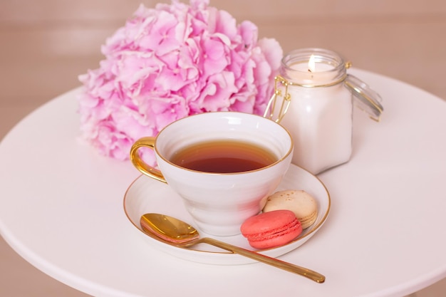 Cup of tea macaroons golden knife and fork and pink hydrangea flower on white table