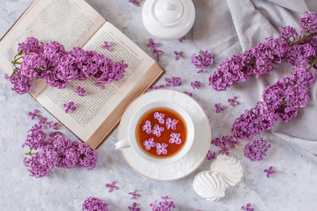 Una tazza di tè, meringa, rami di lillà in fiore e un vecchio libro su uno sfondo vecchio