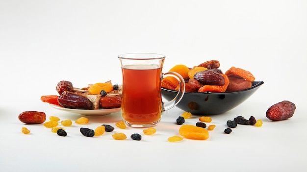 A cup of tea and a mixture of dried fruits in a plate on white