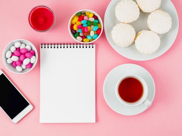 Cup of tea, notepad, mobile and plates of different sweets - marshmallows, lollipops