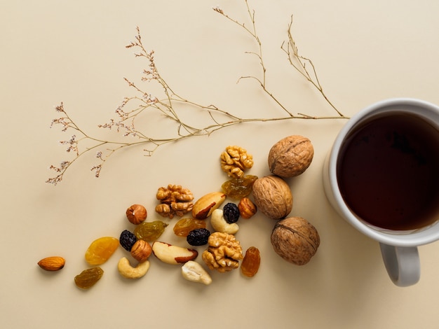 A Cup of tea, nuts and raisins next to dried flowers on a yellow.