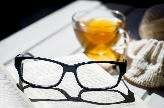 차 한잔, 펼친 책 및 섬 라이트 그림자가있는 안경
