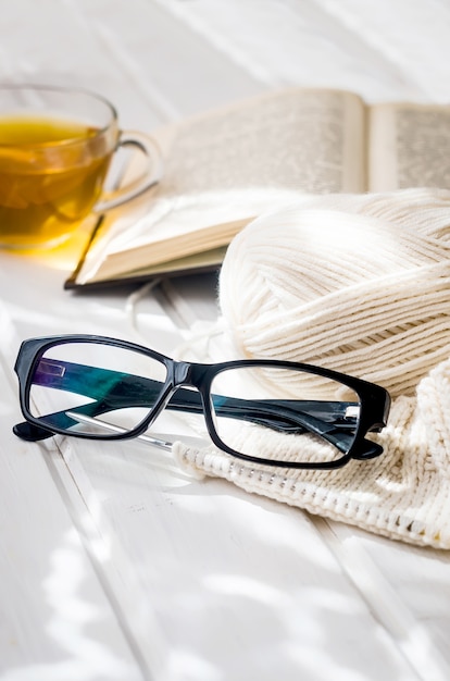 Cup of tea, open book and eyeglasses with sumlight shadow