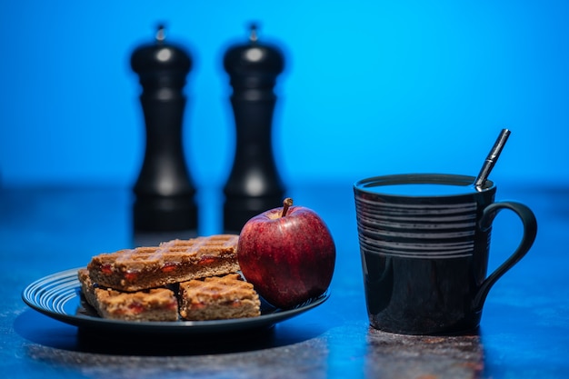 A cup of tea and a plate of cookies and apple standing on the table