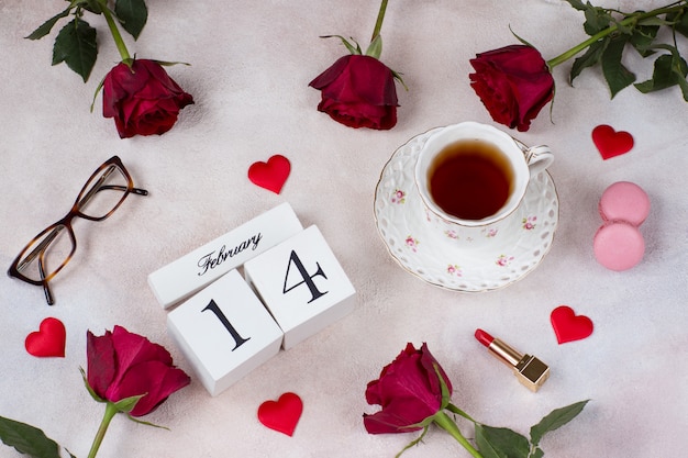 a cup of tea, red roses, macaroons, satin hearts, glasses and a calendar date February 14