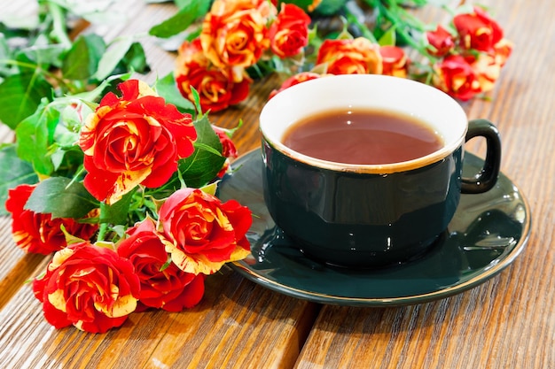 Cup of tea and roses bouquet on wooden table