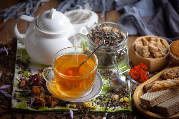 A cup of tea sits on a table next to a teapot with a tea bag and a teapot with a tea bag.