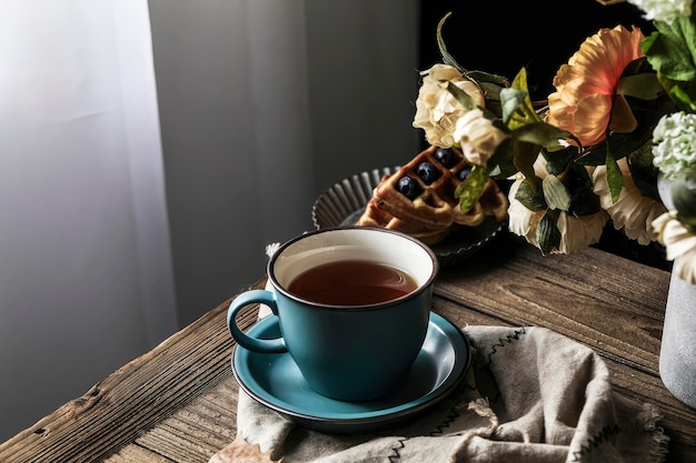 一杯の紅茶がワッフルの隣のテーブルに置かれ、花束が添えられています。コーヒーのビンテージ写真です。