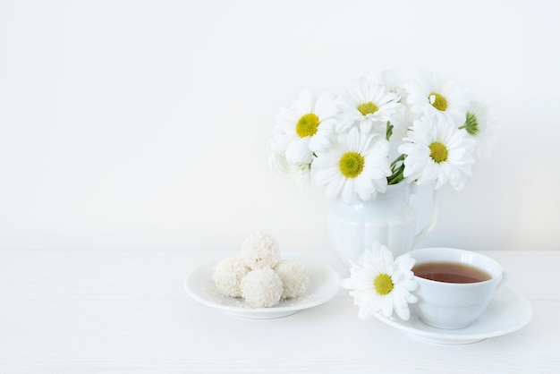 Cup of tea sweets bouquet or chamomile or daisy flowers on a white wooden table Tea and flowers