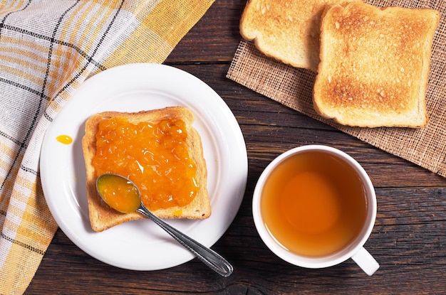 Cup of tea and toast with apricot jam on wooden table top view