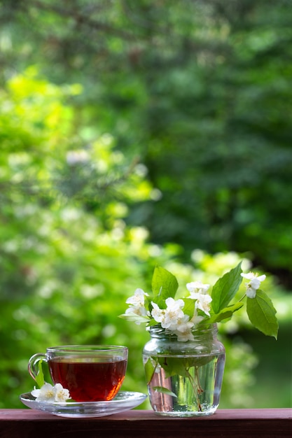 A cup of tea and a vase with sprigs of jasmine.