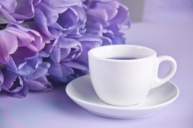 A cup of tea and violet tulips on the table