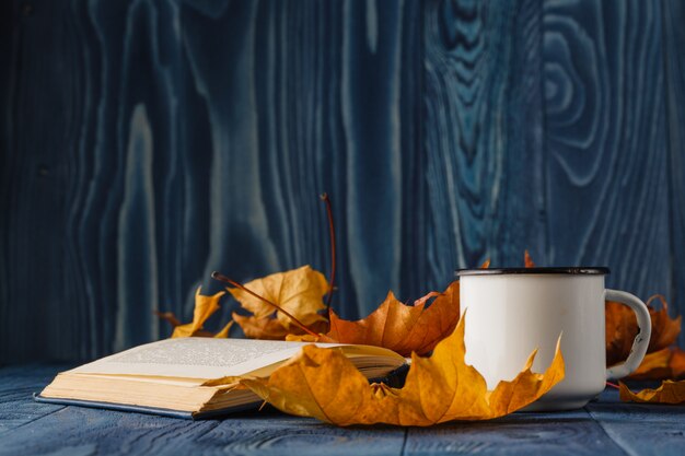 Cup of tea wit old book and autumn leaves on wooden table