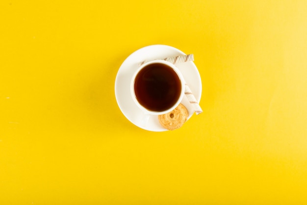 A cup of tea with biscuit on a yellow. top view