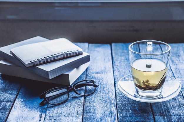 Cup of tea with book and glasses on wooden table