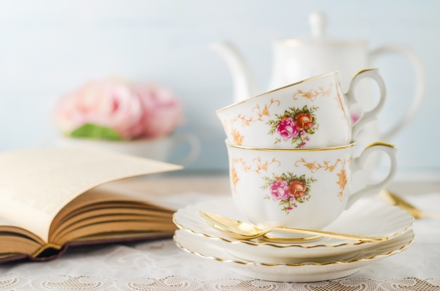 Cup of tea with book, teapot and rose flowers on blue 