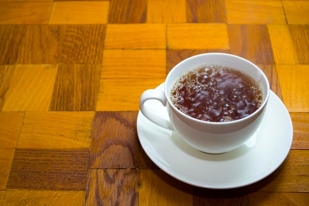 A cup of tea with bubbles stands on a wooden table