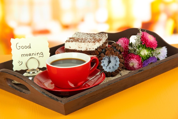 Cup of tea with cakes on wooden tray on table in room