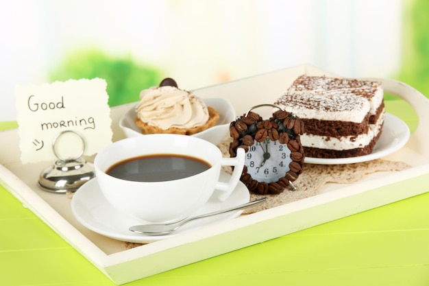 Cup of tea with cakes on wooden tray on table in room