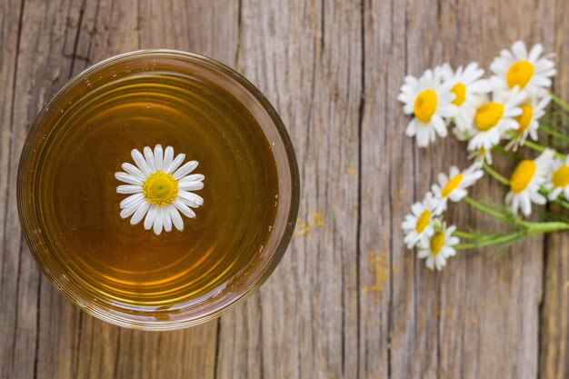 素朴な木製のテーブルにカモミールの花とお茶のカップ。