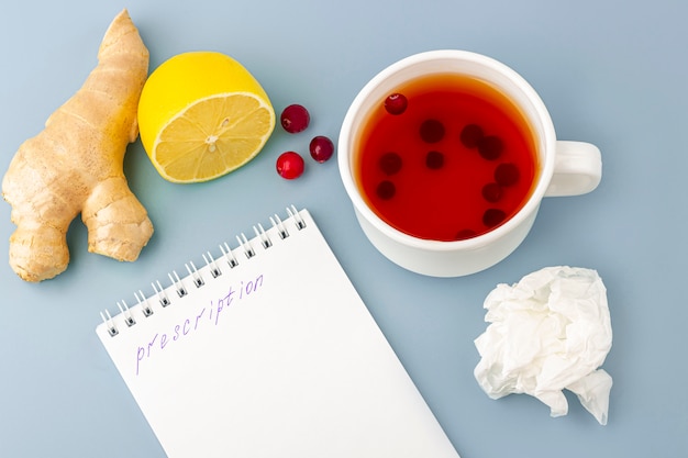 Cup of tea with cranberries, lemon, crumpled napkin, medical mask and prescription on blue