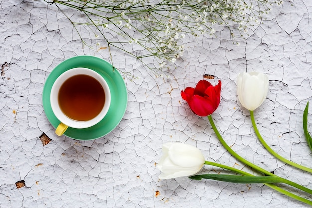 Cup of tea with Floral background with red and white tulips and daisies