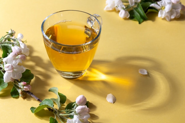 Cup of tea with flowers of apple tree on a light yellow background